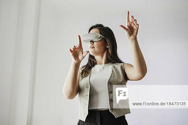 Businesswoman wearing VR glasses gesturing in front of white wall
