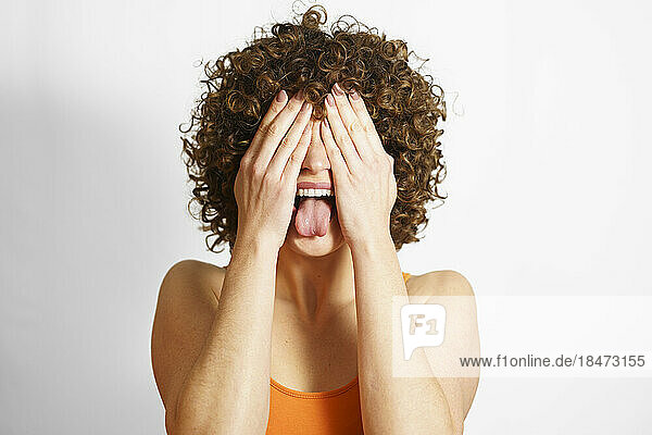 Woman covering face with hands and sticking out tongue