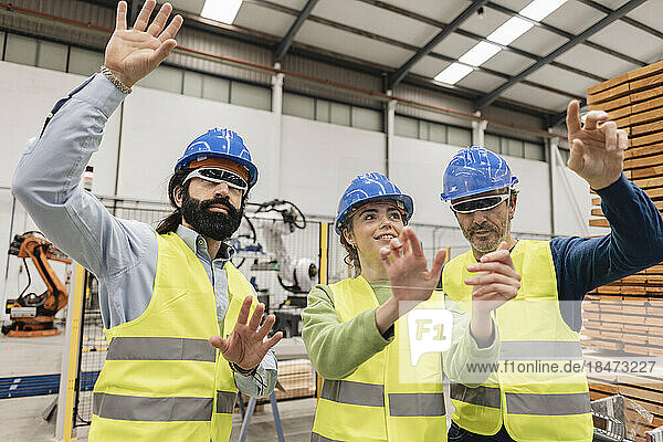 Engineers wearing hardhat gesturing on transparent screen in factory