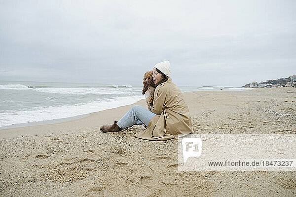 Junge Frau sitzt mit Maltipoo-Hund im Sand am Strand