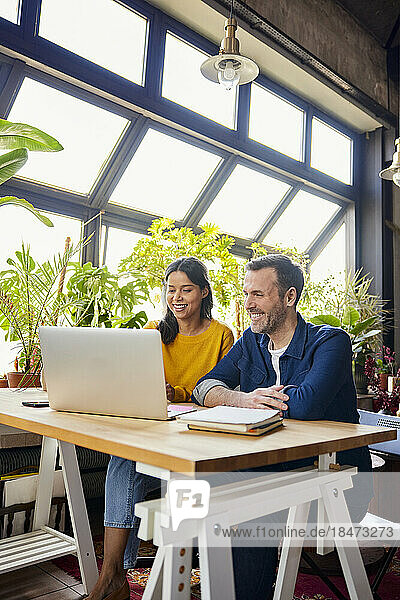 Smiling business colleagues sharing laptop working at loft office