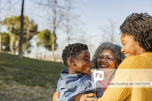 Glückliche ältere Frau trägt Enkel und hat Spaß mit Mutter im Park