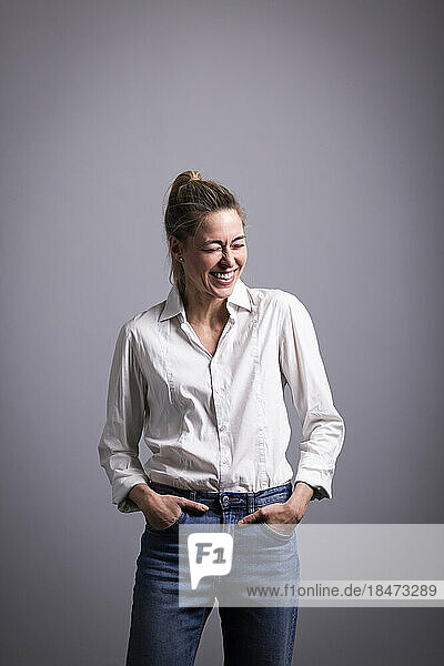 Happy businesswoman standing with hands in pockets against gray background