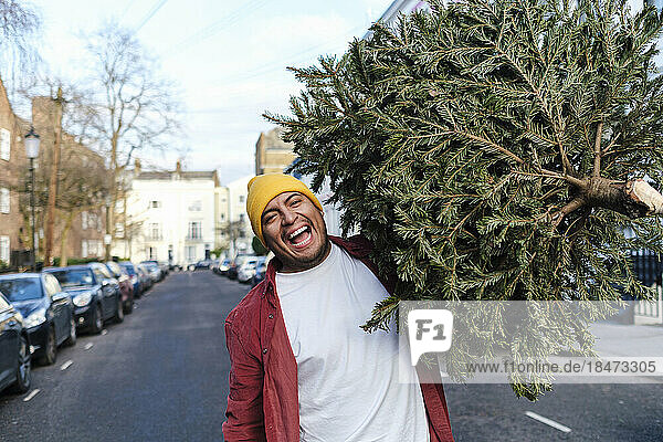 Cheerful man carrying Christmas tree walking on street