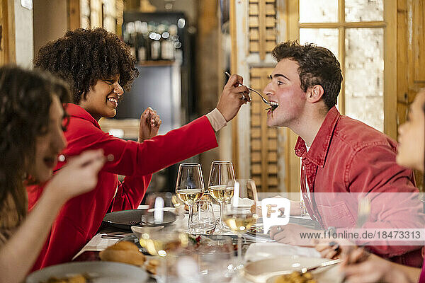 Young woman feeding meal to friend at restaurant