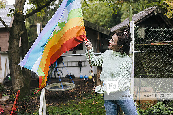 Happy woman standing with rainbow flag in back yard
