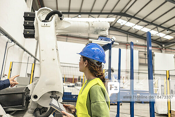 Engineer explaining colleague over robotic arm in factory