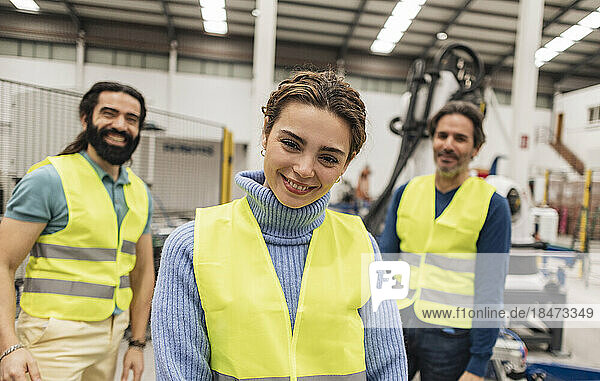 Happy engineers wearing reflective clothing standing with in robotics factory