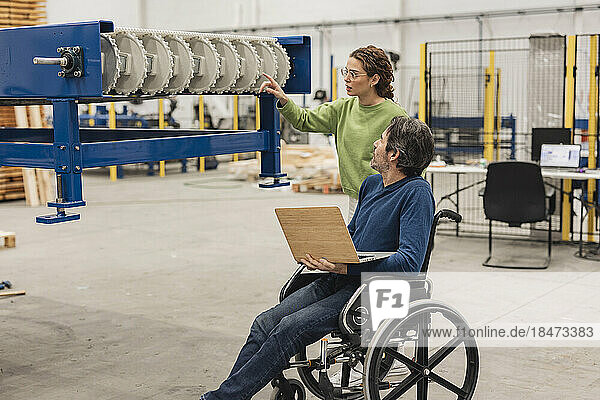 Ingenieur untersucht Maschinenteil mit Kollege im Rollstuhl im Büro