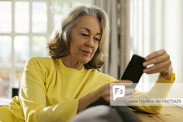 Smiling mature woman using smart phone on sofa at home