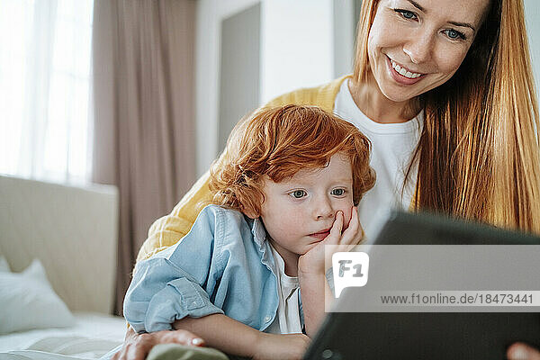 Son watching tablet PC by with mother at home