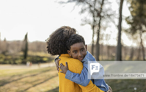 Thoughtful boy embracing mother in park