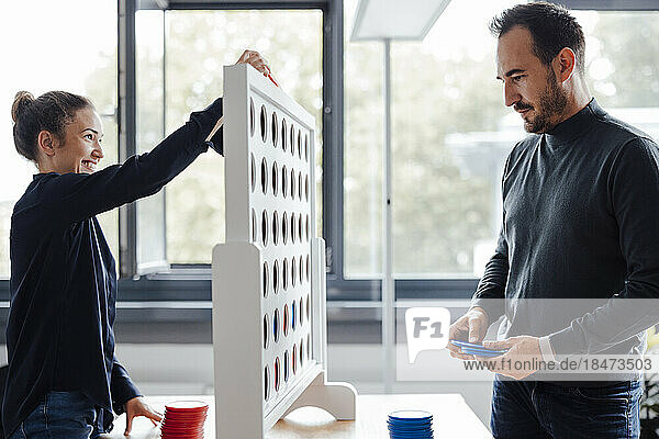 Happy businesswoman with colleague playing connect four dots game in office