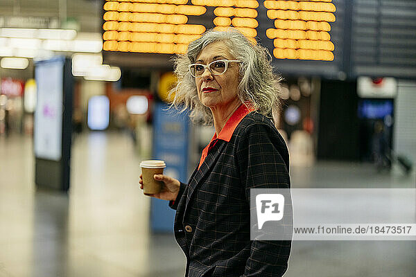 Mature businesswoman with disposable coffee cup standing at station