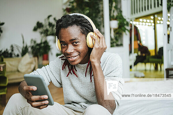 Happy man using smart phone listening to music through headphones at home