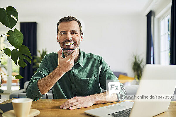 Smiling man talking on the phone while working at home on his laptop