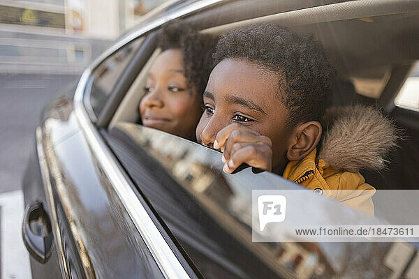 Thoughtful son with mother looking through window in car