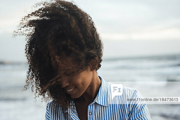 Lächelnde Frau mit lockigem Haar am Strand