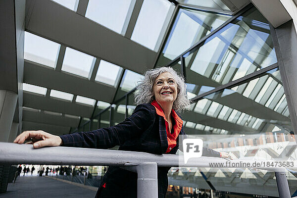 Smiling mature businesswoman leaning on railing at station