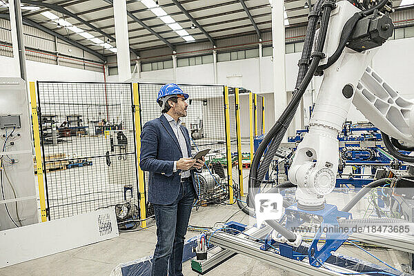 Ingenieur mit Schutzhelm steht mit digitalem Tablet-PC in der Fabrik