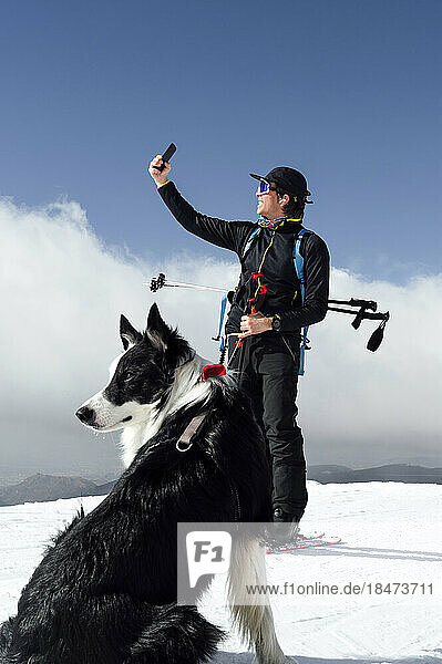Man taking selfie with smart phone with dog sitting on snow