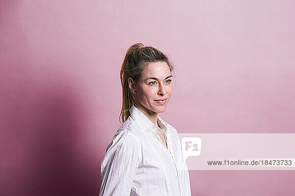 Smiling businesswoman standing against pink background