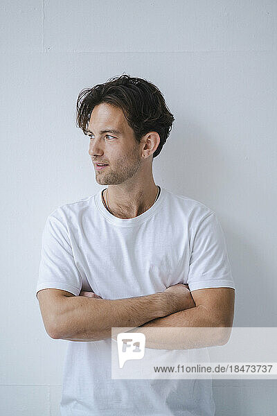 Thoughtful young man with arms crossed leaning on wall