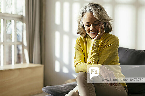 Smiling mature woman with hand on chin sitting at home