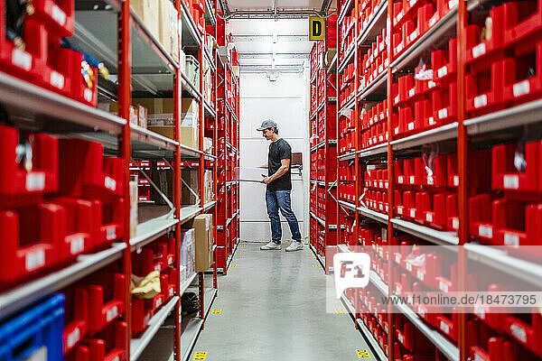 Warehouse worker holding box near racks in factory