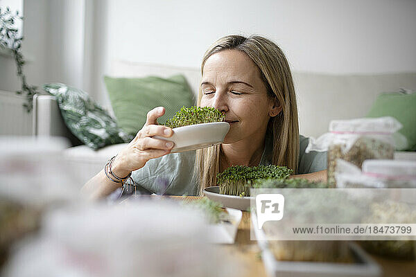 Woman with eyes closed smelling herbs at home