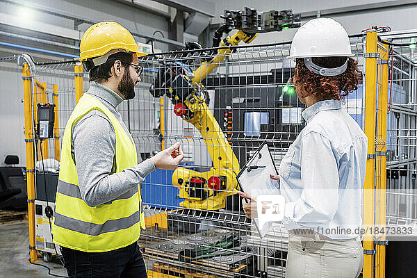 Engineers examining robotic arm in factory