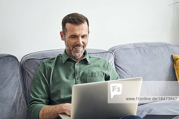 Relaxed man working from home using laptop sitting on the sofa