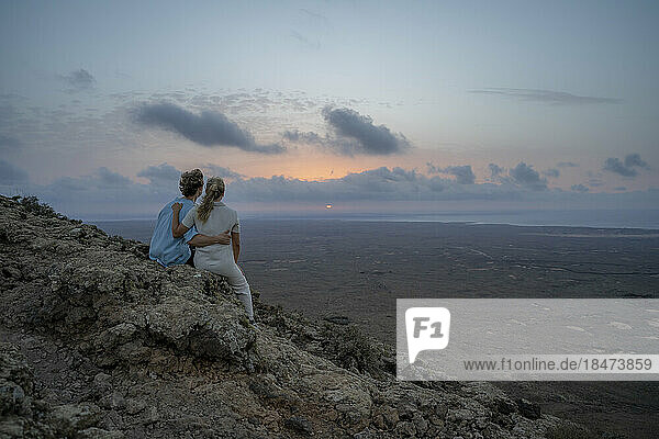 Ein Paar blickt auf den Sonnenuntergang und sitzt auf einem Berg