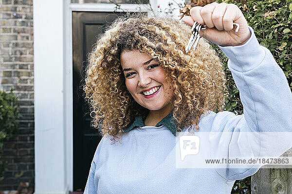 Happy woman with curly hair showing keys of new home