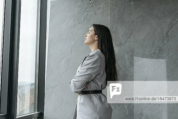 Businesswoman with eyes closed standing near wall at office