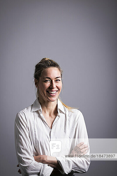Happy mature businesswoman with arms crossed against gray background