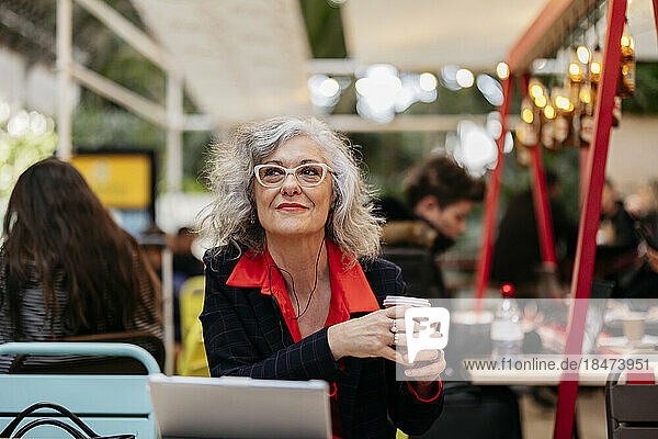 Thoughtful businesswoman sitting with disposable coffee cup in cafe
