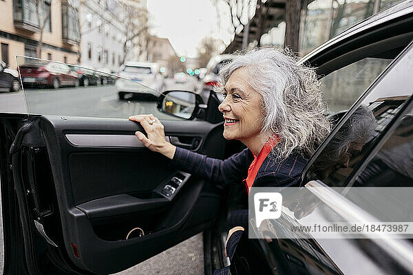 Happy mature businesswoman disembarking from car