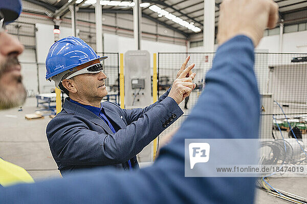 Mature businessman wearing smart glasses with colleague gesturing in industry
