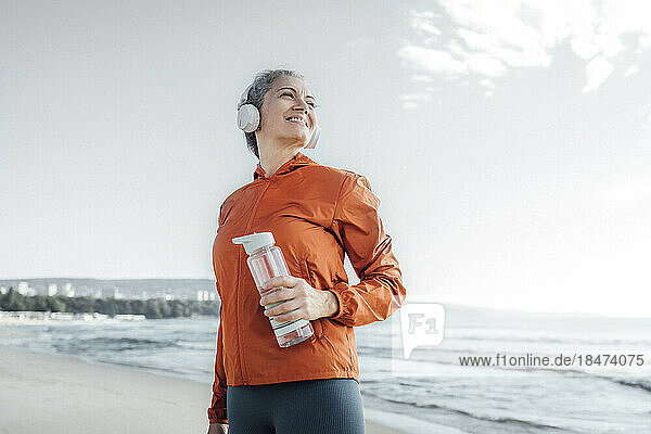 Smiling mature woman with water bottle on beach