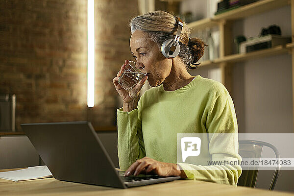 Freelancer drinking water sitting at desk with laptop