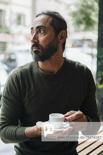 Thoughtful mature man holding coffee cup in cafe