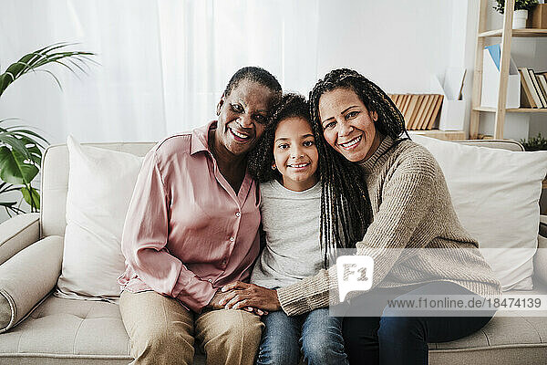 Lächelnde Frau sitzt mit Mutter und Tochter zu Hause auf dem Sofa
