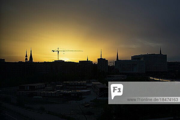 Germany  Hamburg  Silhouettes of city spires and construction crane at sunset