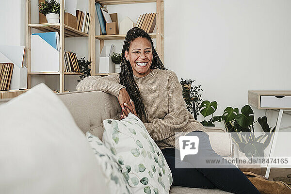 Lächelnde reife Frau sitzt zu Hause auf dem Sofa im Wohnzimmer