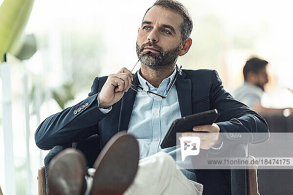 Thoughtful businessman sitting with tablet PC in office