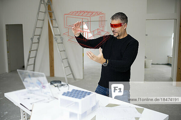 Architect wearing virtual reality simulator examining house model and gesturing at construction site