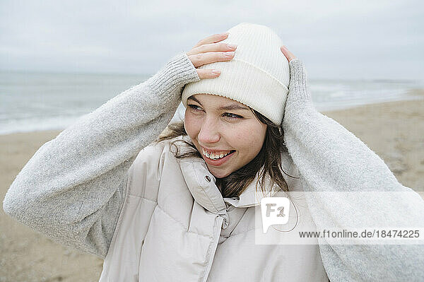 Happy woman adjusting knit hat at beach