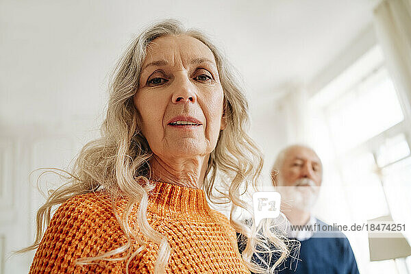 Ältere Frau mit Mann im Hintergrund zu Hause