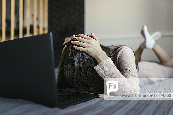 Tired woman lying on bed with laptop at home